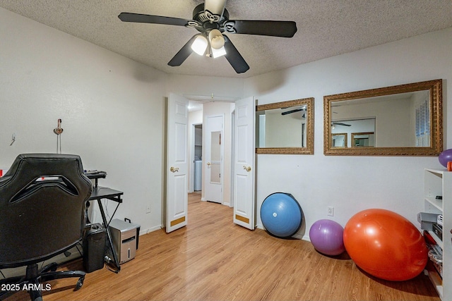 exercise room with ceiling fan, baseboards, light wood finished floors, and a textured ceiling