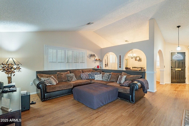 living area with lofted ceiling, an inviting chandelier, wood finished floors, arched walkways, and a textured ceiling