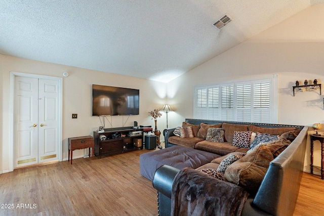 living area with lofted ceiling, visible vents, light wood-type flooring, and a textured ceiling