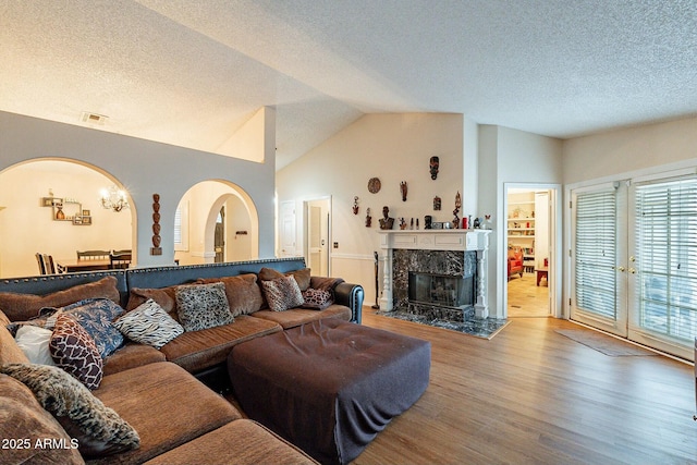 living area featuring visible vents, lofted ceiling, a fireplace, wood finished floors, and a textured ceiling