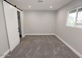 7840 N 7th St Unit 15, Phoenix, AZ 85020 - unfurnished bedroom featuring a barn door, carpet flooring, and recessed lighting
