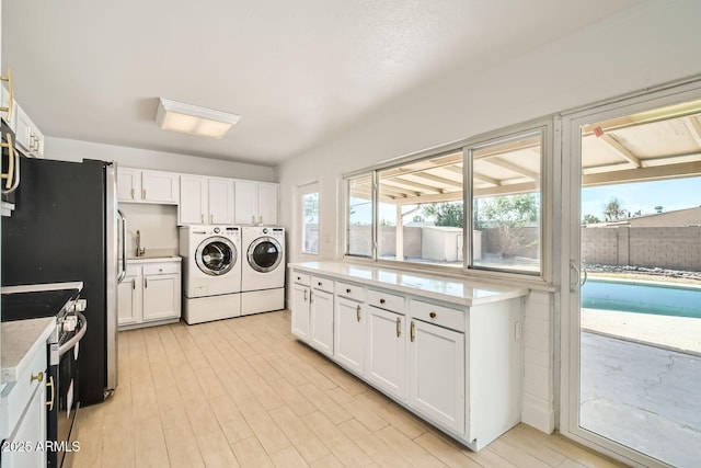 kitchen with washing machine and clothes dryer, appliances with stainless steel finishes, white cabinetry, and light stone counters