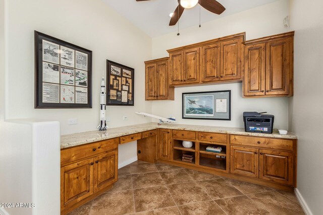 kitchen featuring light stone countertops, built in desk, and ceiling fan