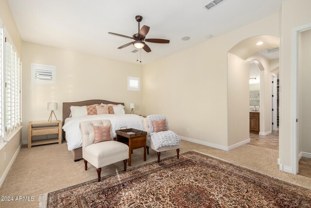 bedroom featuring light carpet, connected bathroom, multiple windows, and ceiling fan