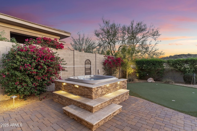 patio terrace at dusk with a fenced backyard and an outdoor hot tub
