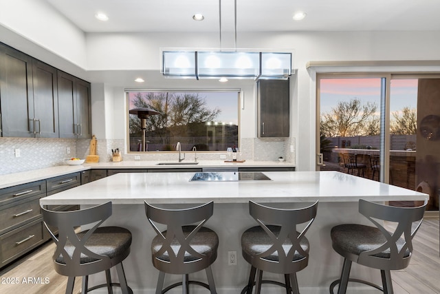 kitchen featuring tasteful backsplash, a sink, black electric stovetop, light wood-type flooring, and a center island
