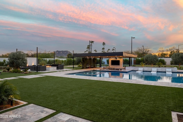 pool at dusk featuring a gazebo, an outdoor living space with a fireplace, a patio area, and a lawn