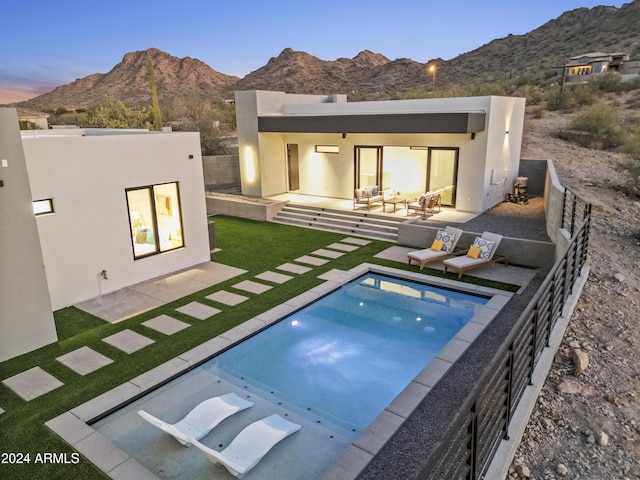 back house at dusk with a mountain view, an outdoor living space, a fenced in pool, and a patio