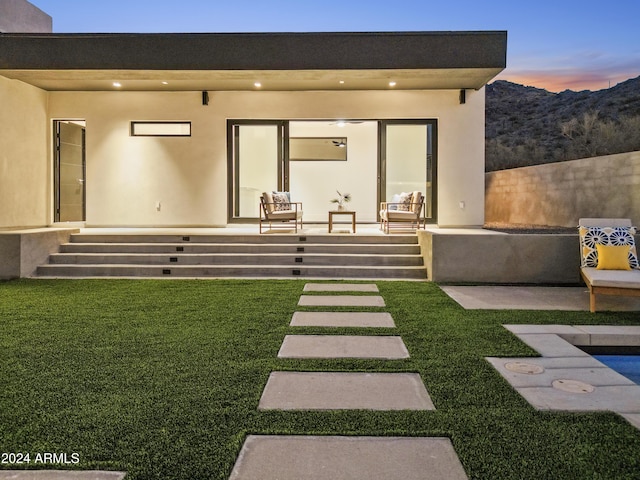 back house at dusk with a patio area and a yard