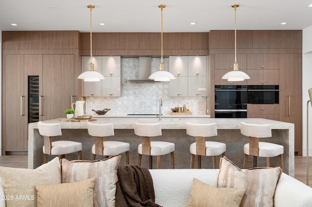 kitchen featuring hanging light fixtures, black double oven, white cabinets, and wall chimney exhaust hood