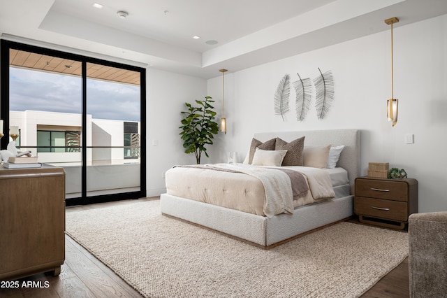 bedroom featuring a raised ceiling, hardwood / wood-style floors, and access to exterior