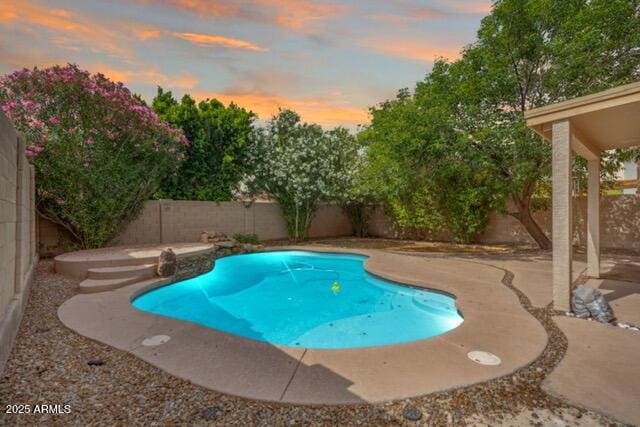 pool at dusk with a fenced backyard and a patio area