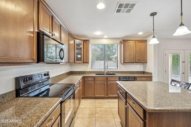 kitchen with black appliances, a sink, brown cabinetry, dark stone counters, and hanging light fixtures
