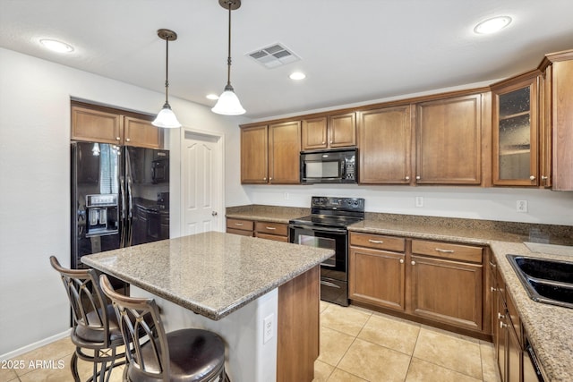 kitchen with black appliances, a kitchen breakfast bar, a center island, brown cabinetry, and hanging light fixtures
