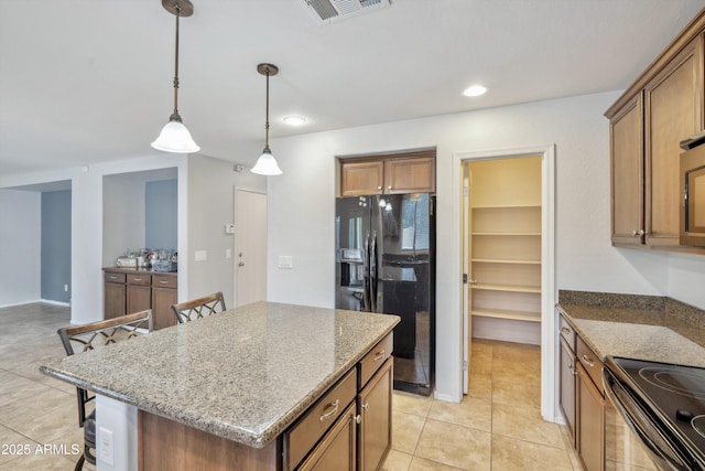 kitchen with black appliances, brown cabinets, light stone countertops, hanging light fixtures, and a kitchen bar