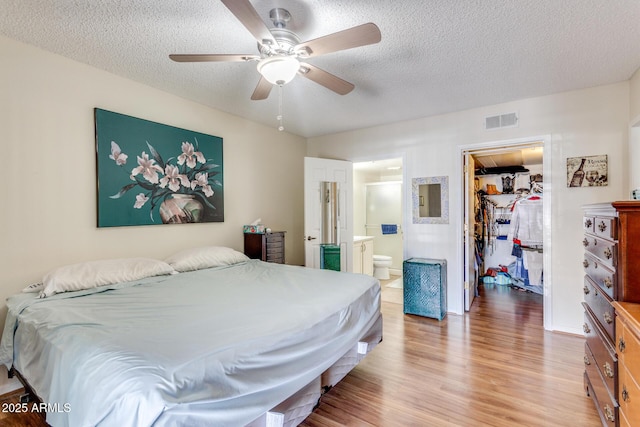 bedroom featuring a walk in closet, a textured ceiling, visible vents, a closet, and light wood-style floors