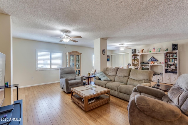 living area with baseboards, a ceiling fan, light wood finished floors, and a textured ceiling