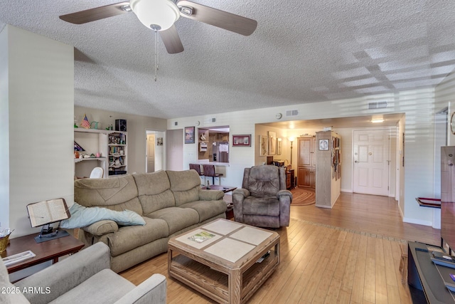 living area featuring ceiling fan, light wood-type flooring, and a textured ceiling