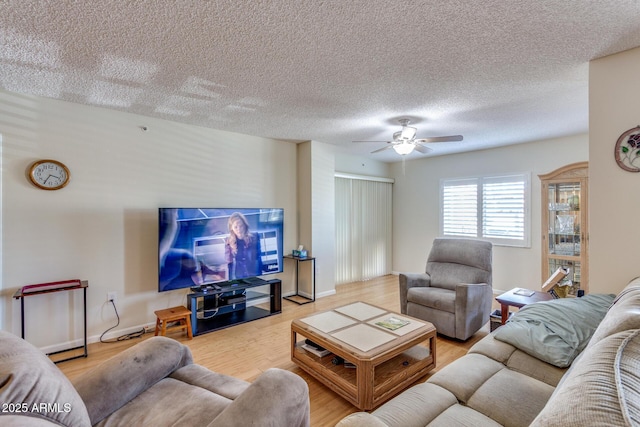 living area with baseboards, a textured ceiling, light wood-style flooring, and ceiling fan