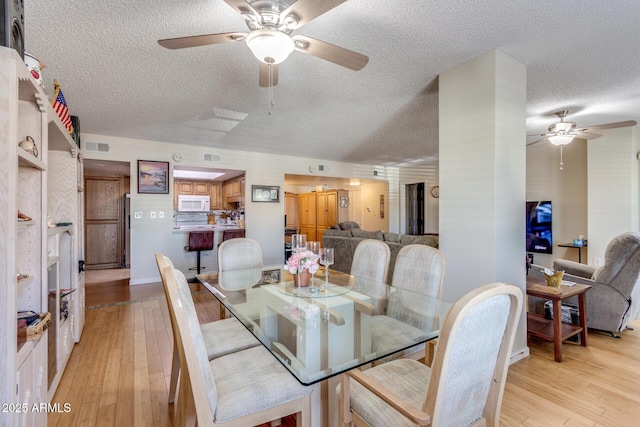 dining room with a ceiling fan, a textured ceiling, and light wood-style flooring