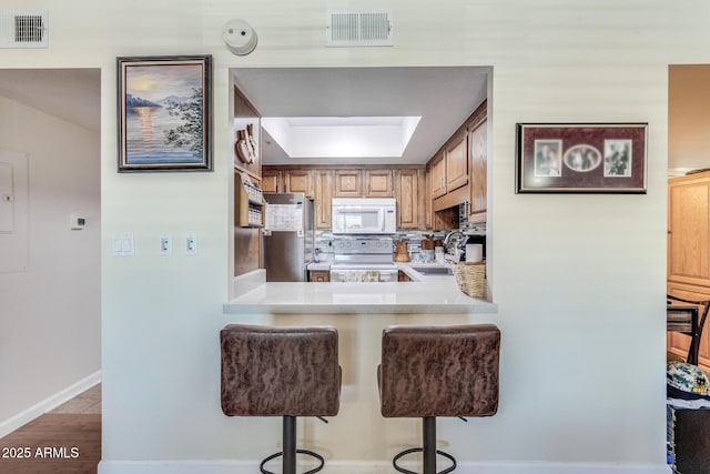 kitchen featuring white appliances, a breakfast bar area, visible vents, and light countertops
