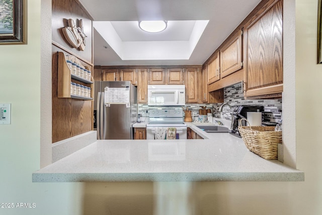 kitchen with light stone countertops, white appliances, a tray ceiling, tasteful backsplash, and a sink