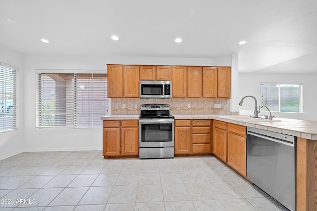 kitchen with sink, kitchen peninsula, decorative backsplash, light tile patterned flooring, and appliances with stainless steel finishes