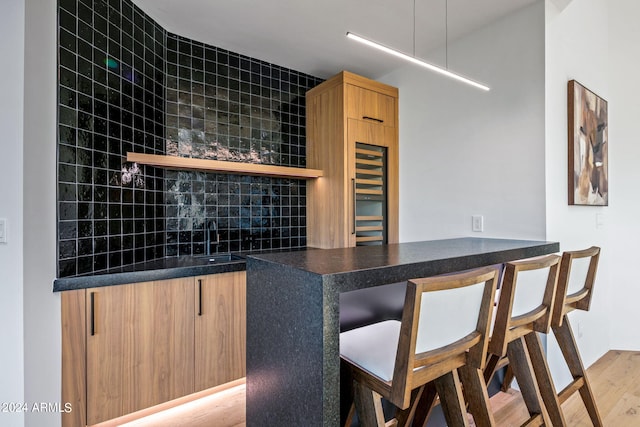 bar featuring sink, decorative backsplash, and light hardwood / wood-style flooring