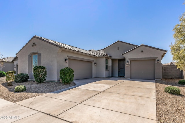 view of front of home featuring a tiled roof, driveway, fence, an attached garage, and stucco siding