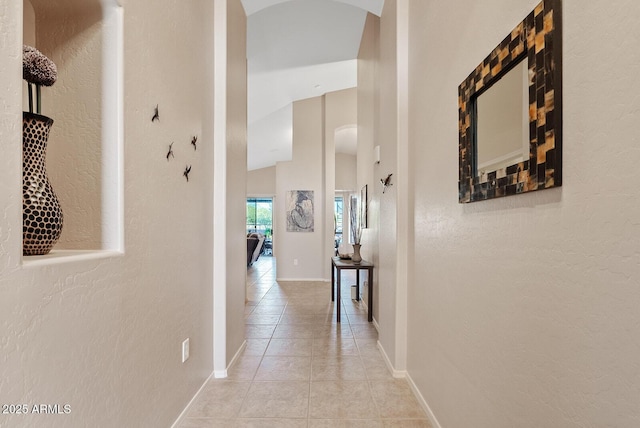corridor with arched walkways, baseboards, a textured wall, and light tile patterned flooring