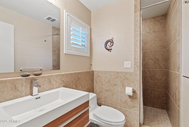 bathroom featuring tile walls, toilet, visible vents, and tiled shower