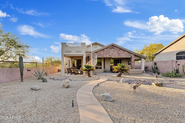 view of front of property featuring a fenced backyard, a patio area, stucco siding, and stairway