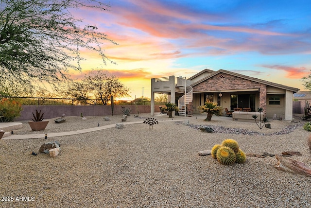 back of house at dusk with fence, a patio, stairway, and stone siding