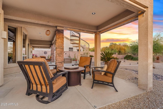 patio terrace at dusk featuring a fenced backyard, an outdoor living space with a fire pit, and stairway