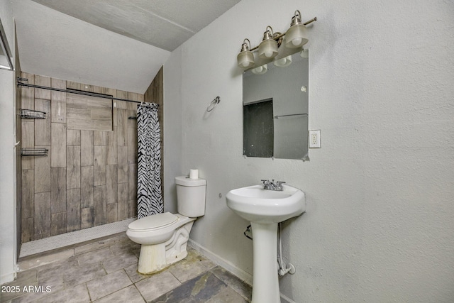 bathroom featuring tiled shower, a sink, toilet, and baseboards