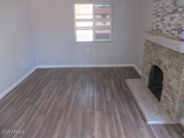 unfurnished living room with baseboards, a fireplace with raised hearth, and wood finished floors