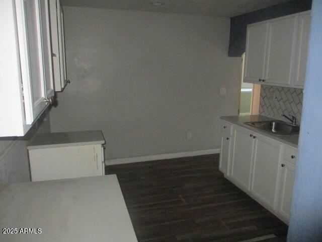 kitchen featuring dark wood finished floors, tasteful backsplash, white cabinetry, a sink, and baseboards