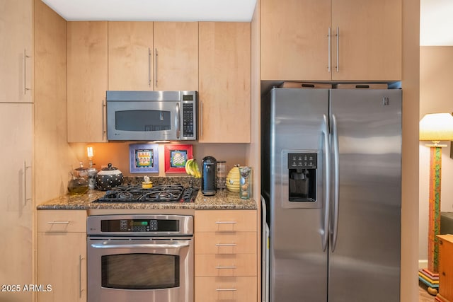 kitchen with light brown cabinetry, appliances with stainless steel finishes, and dark stone countertops