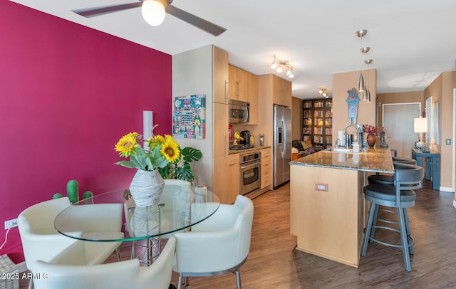 kitchen with wood-type flooring, kitchen peninsula, sink, appliances with stainless steel finishes, and a kitchen breakfast bar