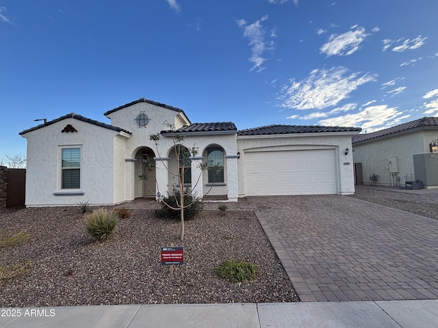 mediterranean / spanish home featuring an attached garage, a tile roof, decorative driveway, and stucco siding