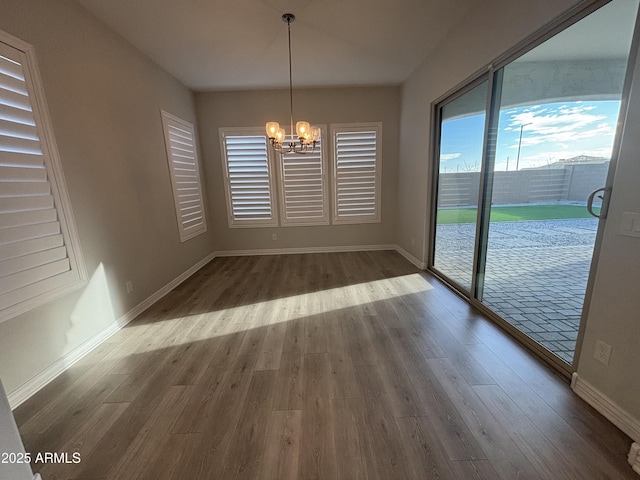 unfurnished dining area with wood finished floors, baseboards, and an inviting chandelier