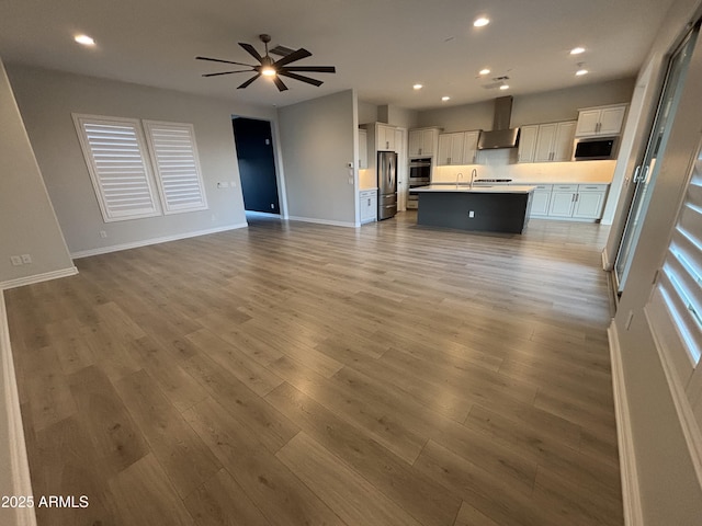 kitchen with wall chimney range hood, stainless steel appliances, light wood finished floors, and open floor plan