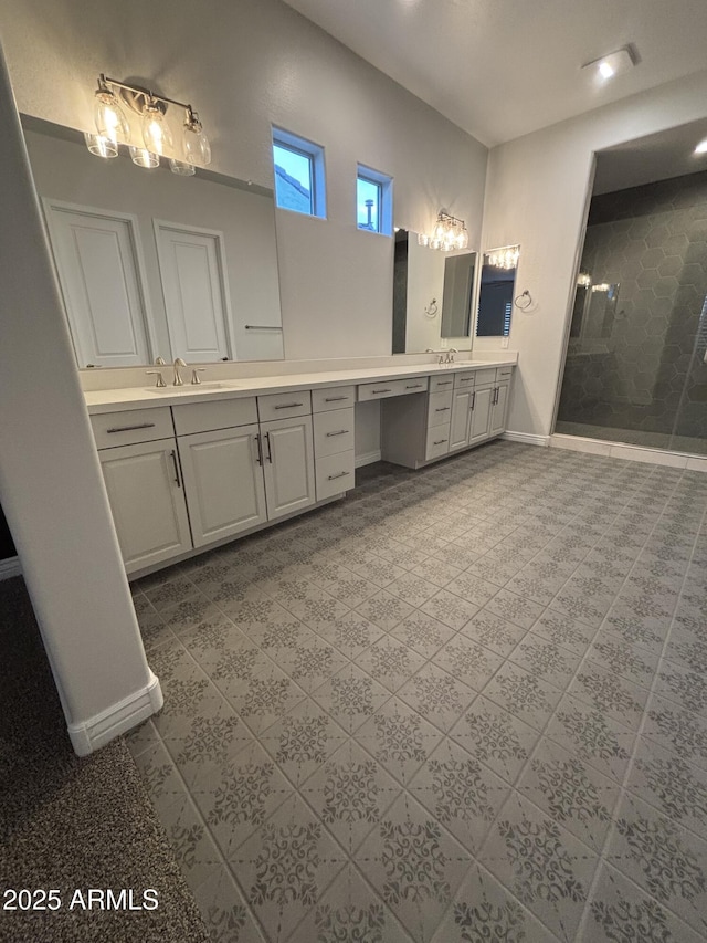 full bath featuring a sink, two vanities, a tile shower, and baseboards