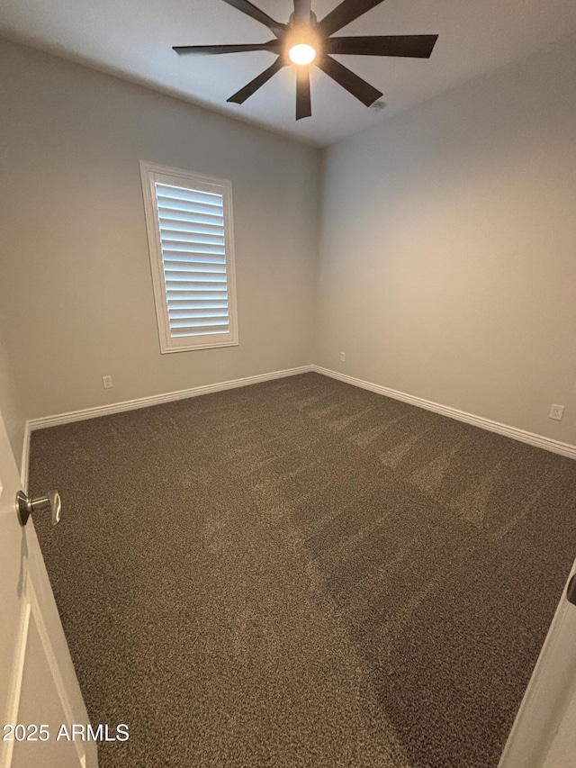 empty room featuring baseboards, dark carpet, and a ceiling fan