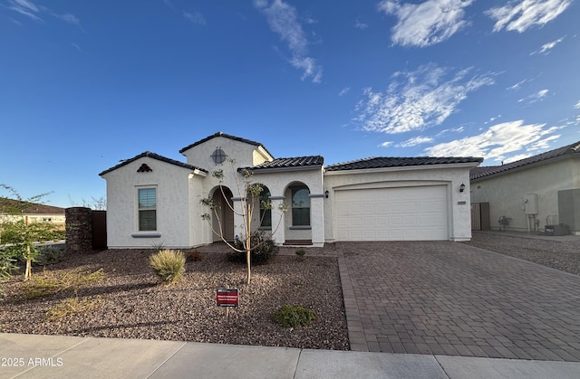 mediterranean / spanish-style home featuring decorative driveway, a tiled roof, an attached garage, and stucco siding