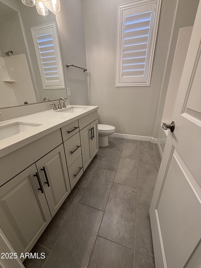 full bath featuring double vanity, a sink, toilet, and baseboards