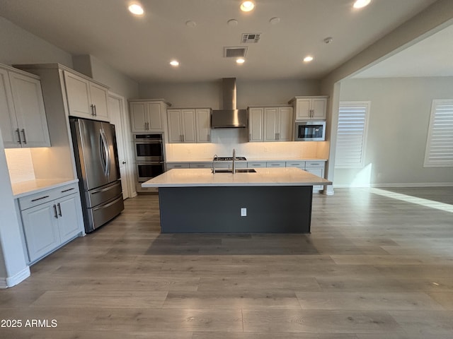 kitchen with visible vents, decorative backsplash, appliances with stainless steel finishes, wall chimney range hood, and a sink