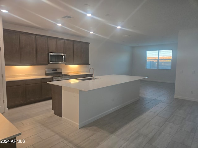 kitchen featuring dark brown cabinetry, sink, an island with sink, and stainless steel appliances