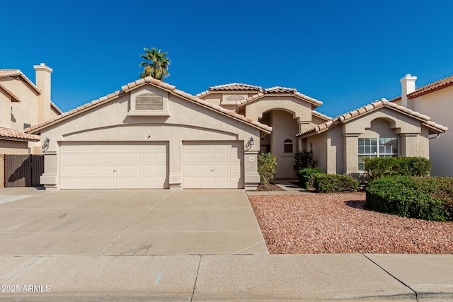 mediterranean / spanish house featuring a tiled roof, stucco siding, an attached garage, and driveway