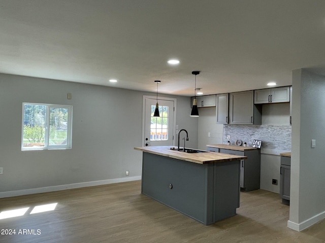 kitchen with gray cabinetry, a center island with sink, tasteful backsplash, light wood-type flooring, and sink